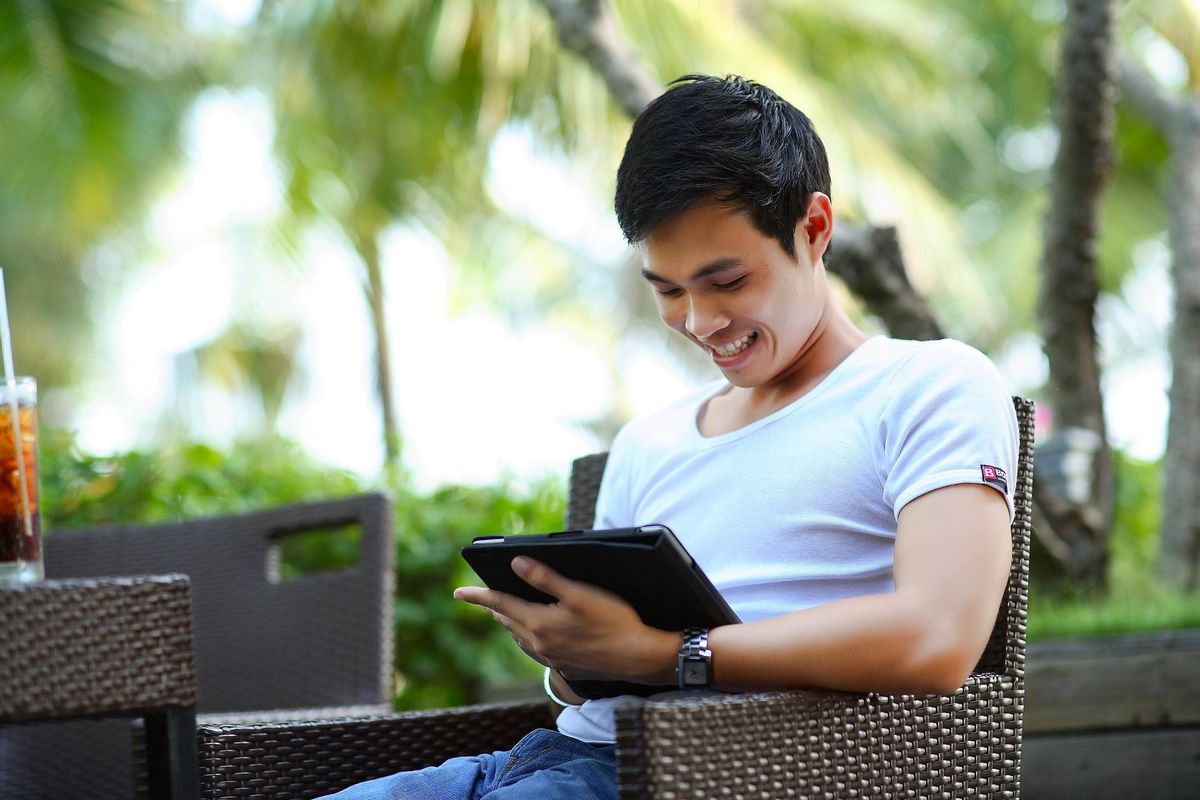 Investmentfonds kaufen - Glücklicher junger Mann mit Tablet auf einer Terrasse im Grünen sitzend